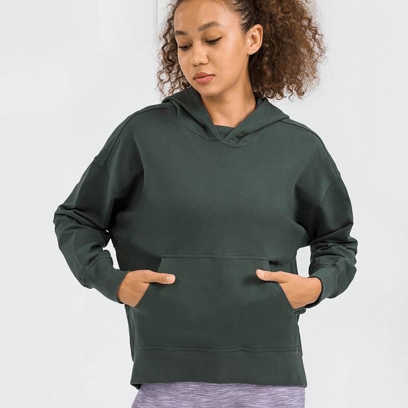 Woman wearing dark green batwing sleeve hoodie for running, featuring loose fit and front pocket, perfect for outdoor activities.